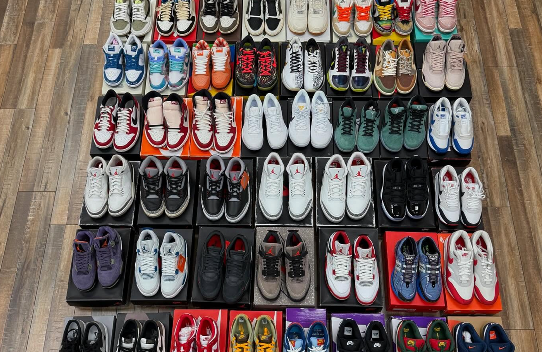 Top view of various Jordans, Nikes, and Travis Scott sneakers neatly arranged in rows on a wooden floor with some pairs on shoeboxes, showcasing diverse sneaker styles and colors.