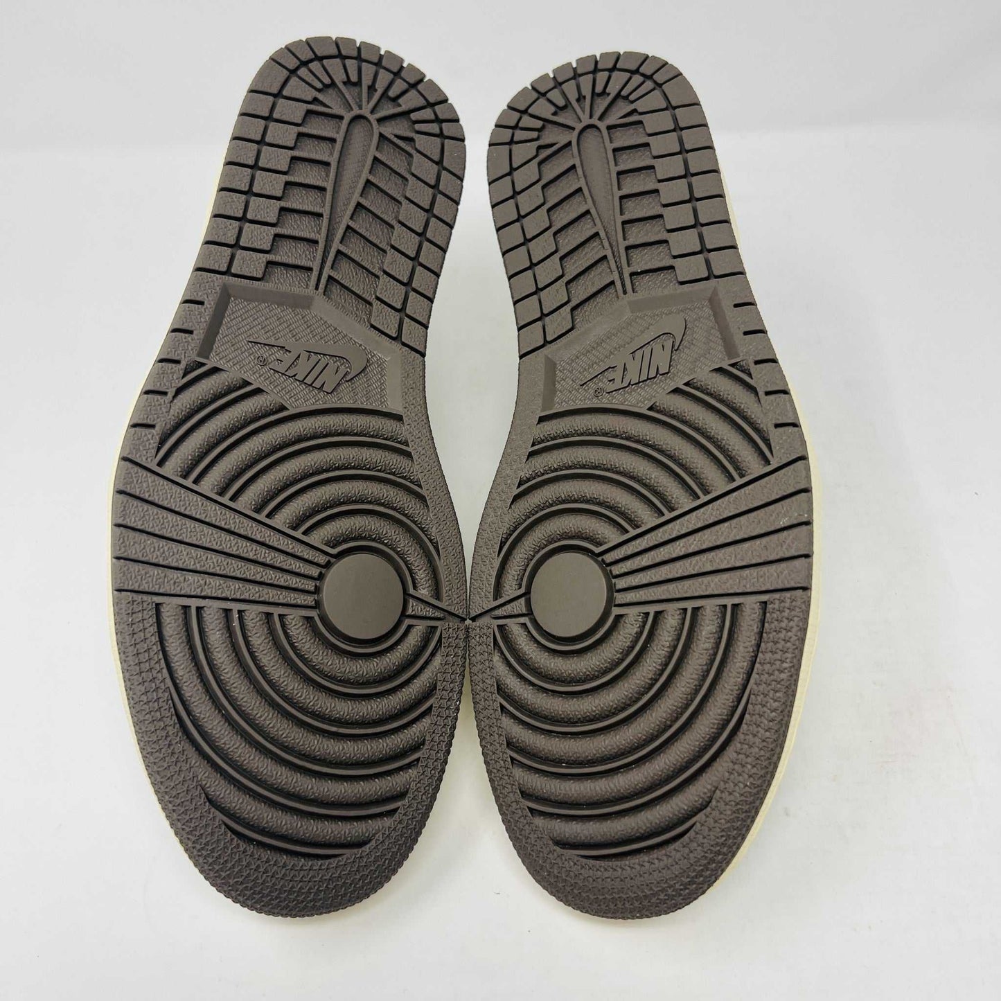 A brand new, 100% authentic pair of Jordan 1 Low Travis Scott Reverse Mocha sneakers in white, gray, and brown sit atop their matching box. The shoes feature a large swoosh on the side, while the box displays the Jordan logo and reads 1985 Air Jordan.