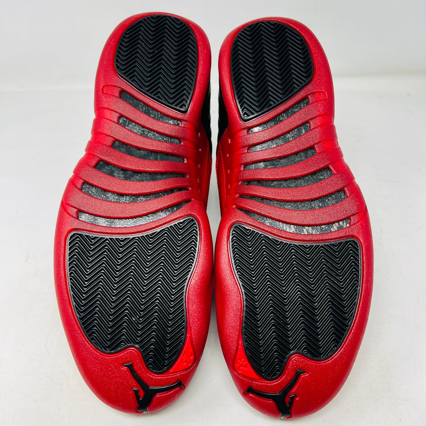 The Jordan 12 Retro Flu Game (2025) athletic shoe in black and red, brand new and pristine, sits atop an immaculate orange-and-black Nike box. It features a textured design with JUMPMAN embossed on its high-top style, perfectly enhancing this stylish accessory from the Jordan brand.