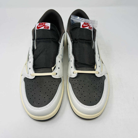 A brand new, 100% authentic pair of Jordan 1 Low Travis Scott Reverse Mocha sneakers in white, gray, and brown sit atop their matching box. The shoes feature a large swoosh on the side, while the box displays the Jordan logo and reads 1985 Air Jordan.