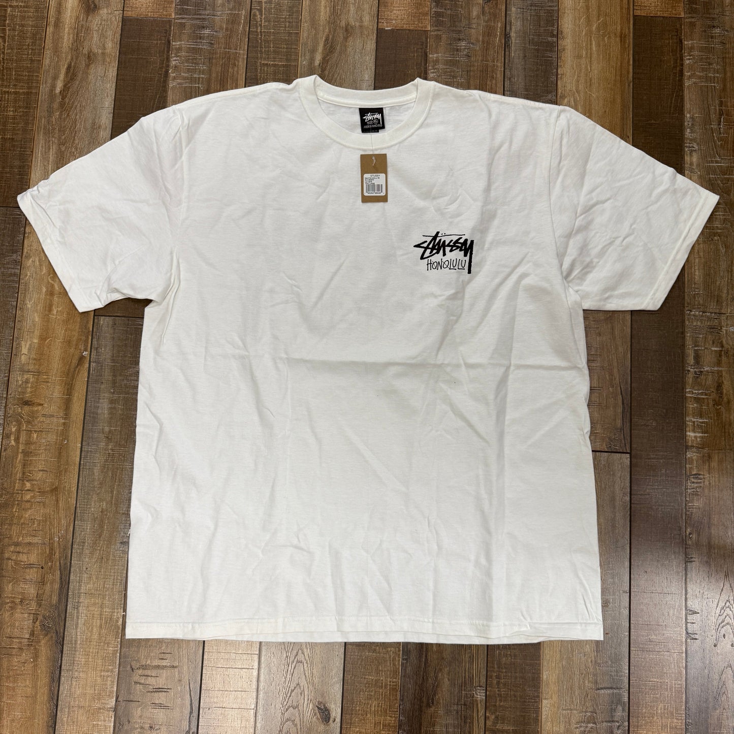Stussy Honolulu T-Shirt White, brand new condition displayed on wooden floor.