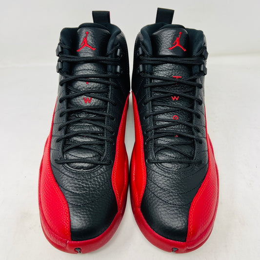 The Jordan 12 Retro Flu Game (2025) athletic shoe in black and red, brand new and pristine, sits atop an immaculate orange-and-black Nike box. It features a textured design with JUMPMAN embossed on its high-top style, perfectly enhancing this stylish accessory from the Jordan brand.