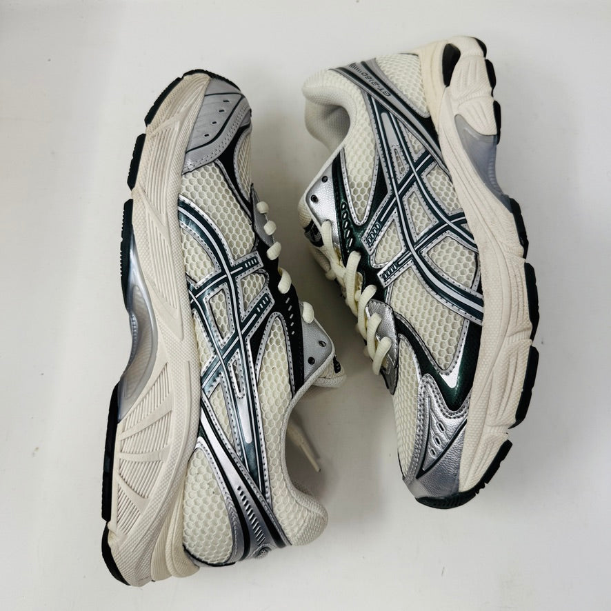 The ASICS GT-2160 Kith Cream Scarab is displayed on a brown box with two spare lace sets, striped and white, offering versatility. An Ortholite tag emphasizes comfort while its clean white and black uppers ensure it complements any outfit effortlessly.