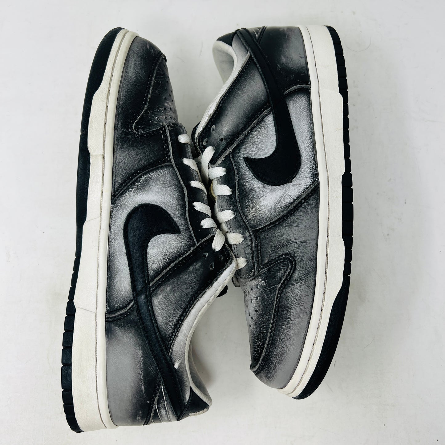 A pair of worn black and white Nike Dunk Low Haze sneakers with visible scuff marks rest on an orange Nike shoebox labeled size 10.5, featuring product details.