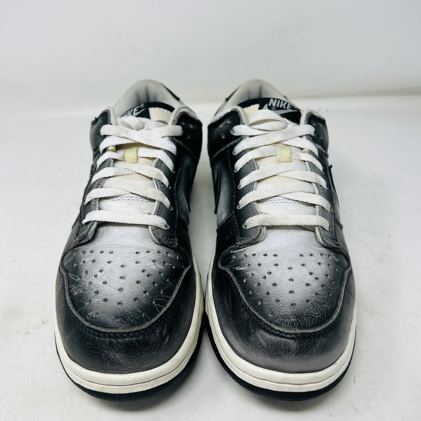 A pair of worn black and white Nike Dunk Low Haze sneakers with visible scuff marks rest on an orange Nike shoebox labeled size 10.5, featuring product details.