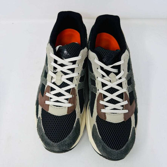 A sleek ASICS Gel-1130 MK-II HAL Studio Forest sits on its box, displaying black and brown mesh with suede accents. Distinctive orange detailing highlights the heel, while an extra brown laces bag accompanies it, enhancing its authentic athletic style.