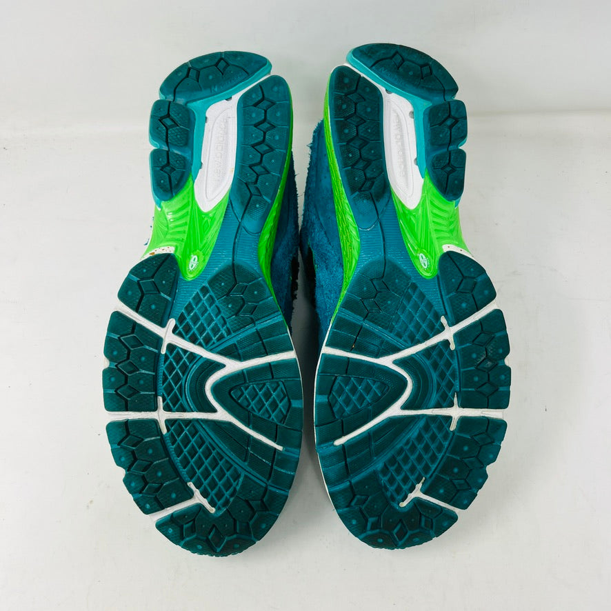 A pair of New Balance 2002R by Salehe Bembury, in colorful teal, pink, and green accents, sits atop a shoebox. Two extra lace setsāpink and greenāare in front. The shoebox label details the size and style; the box is in good condition with a clean design.