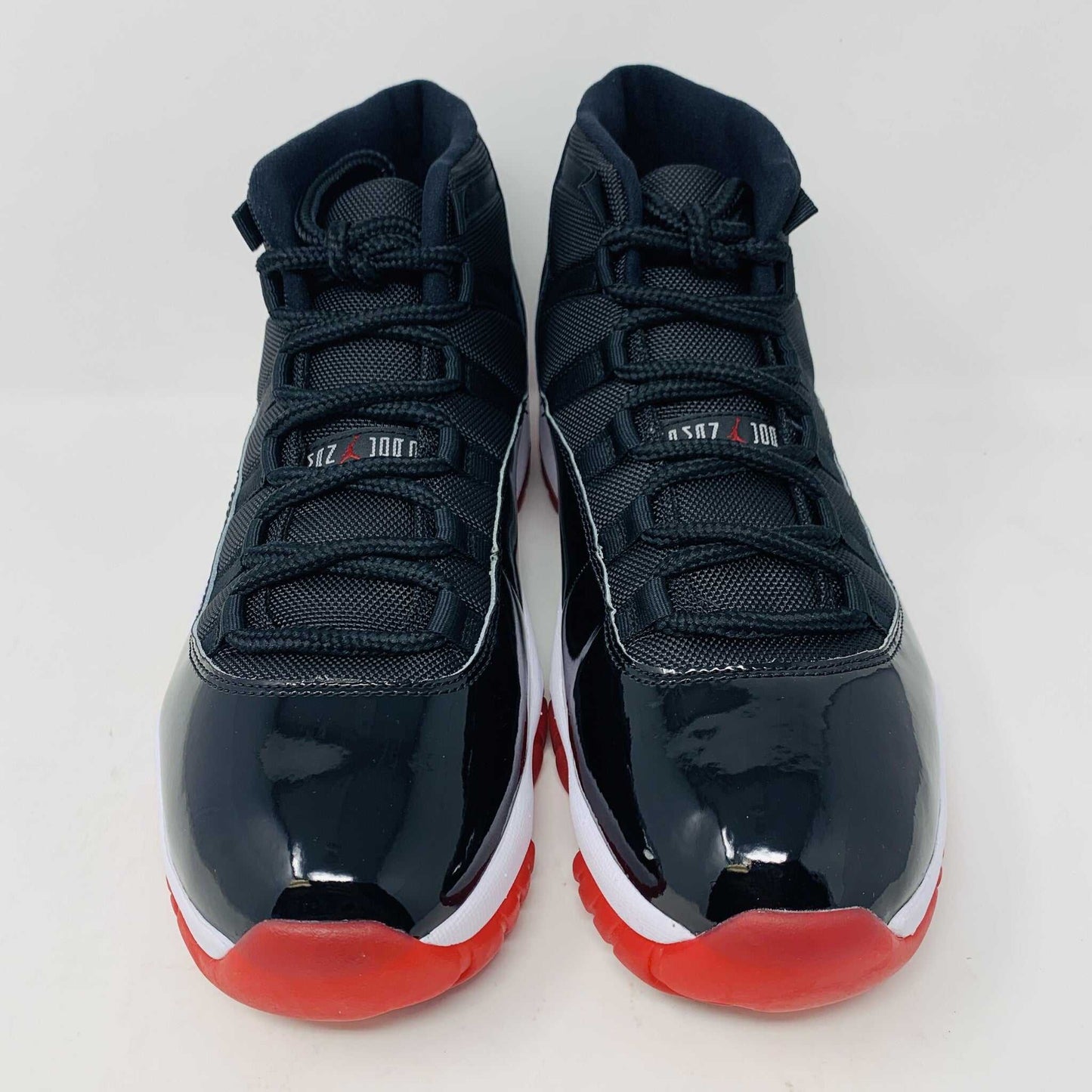 The brand new Jordan 11 Bred 2019 features a black and red high-top design with glossy accents, striking red soles, and a bold red Jumpman logo. It sits atop an orange and black Nike shoebox, exuding style and performance.