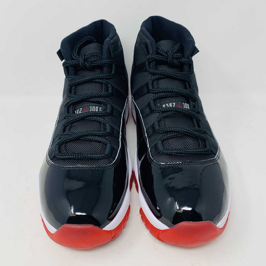 The brand new Jordan 11 Bred 2019 features a black and red high-top design with glossy accents, striking red soles, and a bold red Jumpman logo. It sits atop an orange and black Nike shoebox, exuding style and performance.