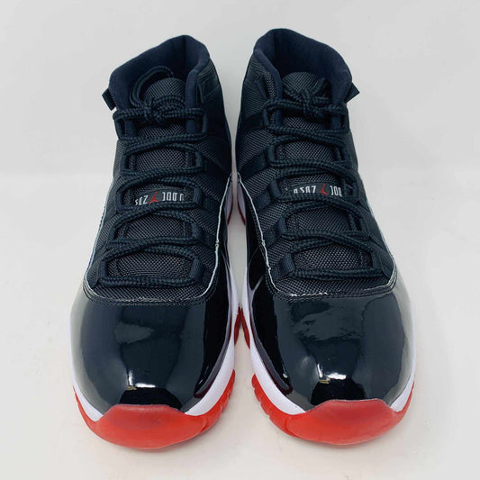 The brand new Jordan 11 Bred 2019 features a black and red high-top design with glossy accents, striking red soles, and a bold red Jumpman logo. It sits atop an orange and black Nike shoebox, exuding style and performance.
