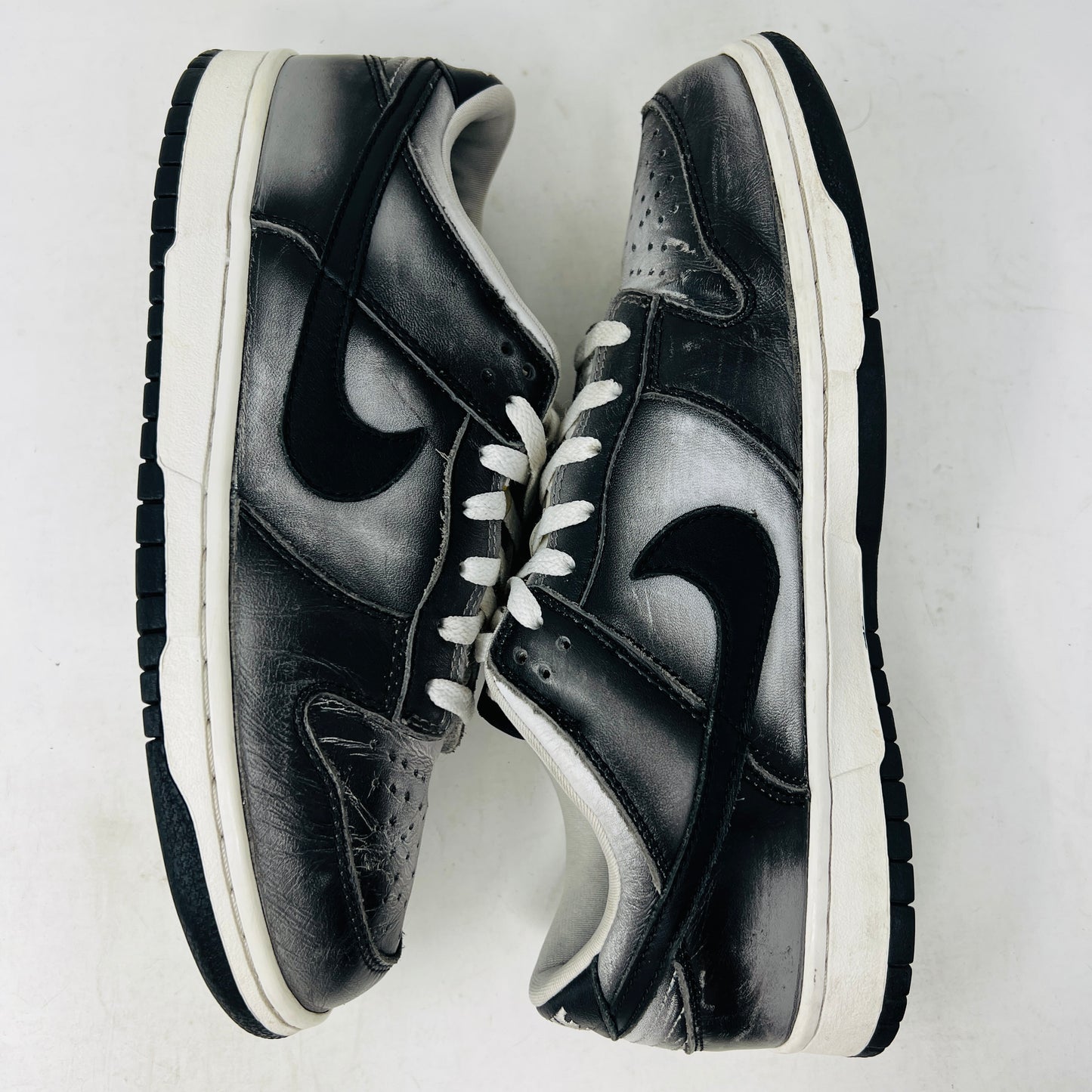 A pair of worn black and white Nike Dunk Low Haze sneakers with visible scuff marks rest on an orange Nike shoebox labeled size 10.5, featuring product details.