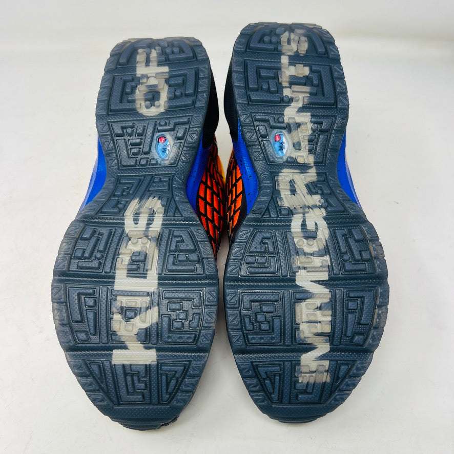 The Nike Air Max Sunder SP Kids of Immigrants Sunrise sneakers in bright orange and black feature a grid pattern with blue accents. An authentic swoosh and a circular K-I design mark the shoes and the orange box, highlighting their uniqueness.