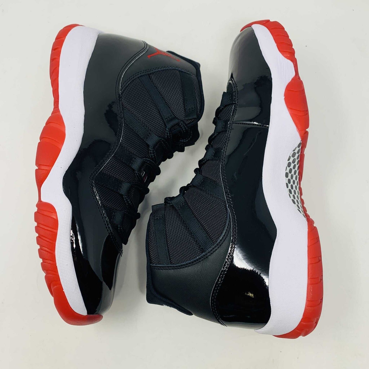 The brand new Jordan 11 Bred 2019 features a black and red high-top design with glossy accents, striking red soles, and a bold red Jumpman logo. It sits atop an orange and black Nike shoebox, exuding style and performance.