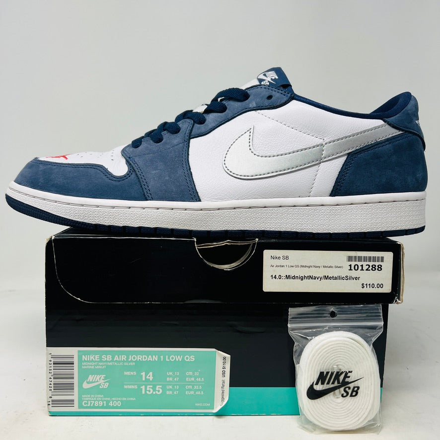 The Jordan 1 Low SB Midnight Navy sneakers, with white and navy panels and a side Nike swoosh, are displayed on a pristine shoebox. A spare set of white laces featuring the Nike SB logo in Metallic Silver is also included.