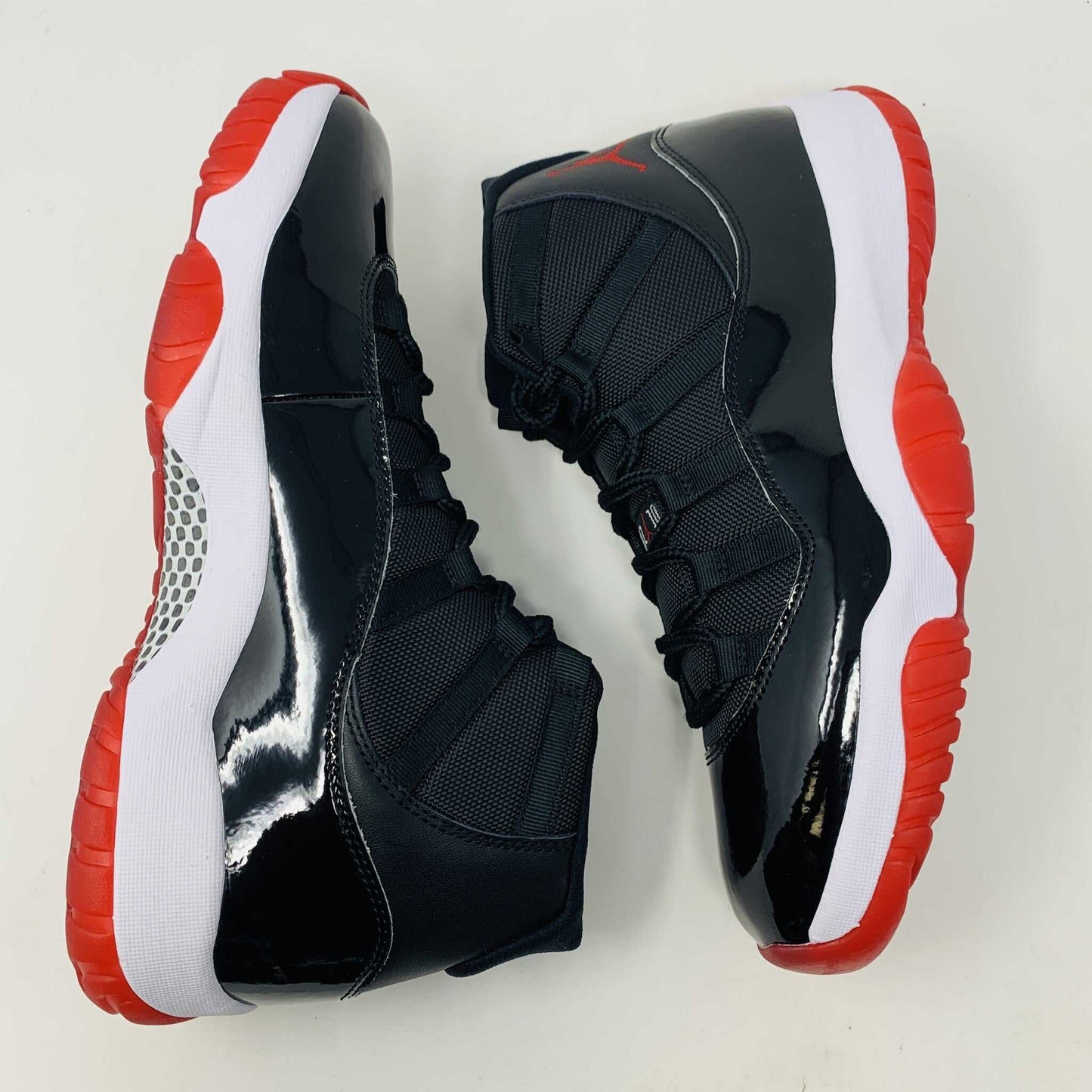 The brand new Jordan 11 Bred 2019 features a black and red high-top design with glossy accents, striking red soles, and a bold red Jumpman logo. It sits atop an orange and black Nike shoebox, exuding style and performance.