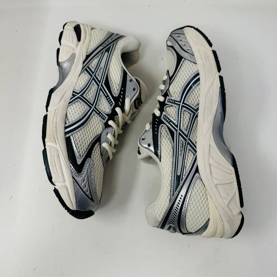 The ASICS GT-2160 Kith Cream Scarab is displayed on a brown box with two spare lace sets, striped and white, offering versatility. An Ortholite tag emphasizes comfort while its clean white and black uppers ensure it complements any outfit effortlessly.