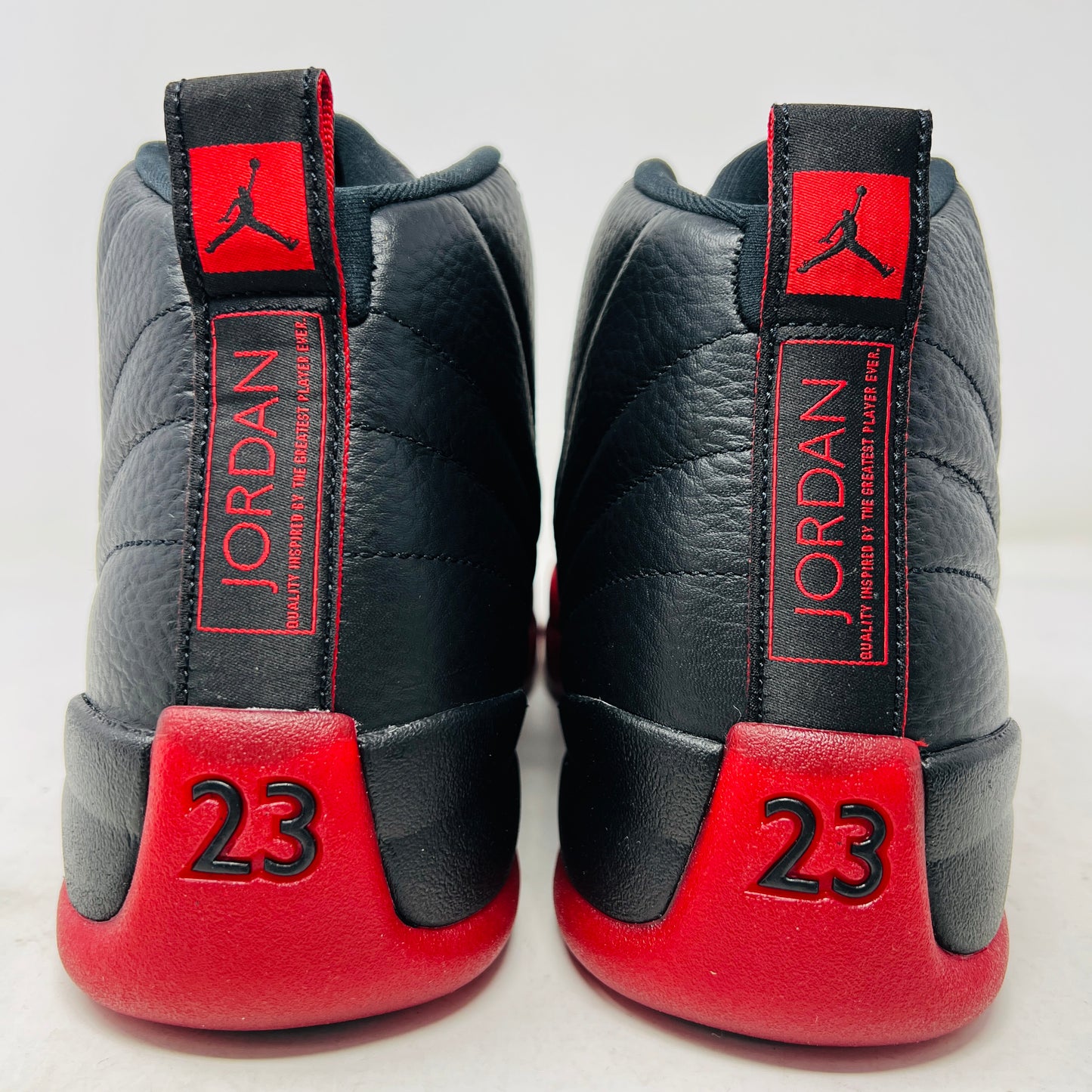 The Jordan 12 Retro Flu Game (2025) athletic shoe in black and red, brand new and pristine, sits atop an immaculate orange-and-black Nike box. It features a textured design with JUMPMAN embossed on its high-top style, perfectly enhancing this stylish accessory from the Jordan brand.
