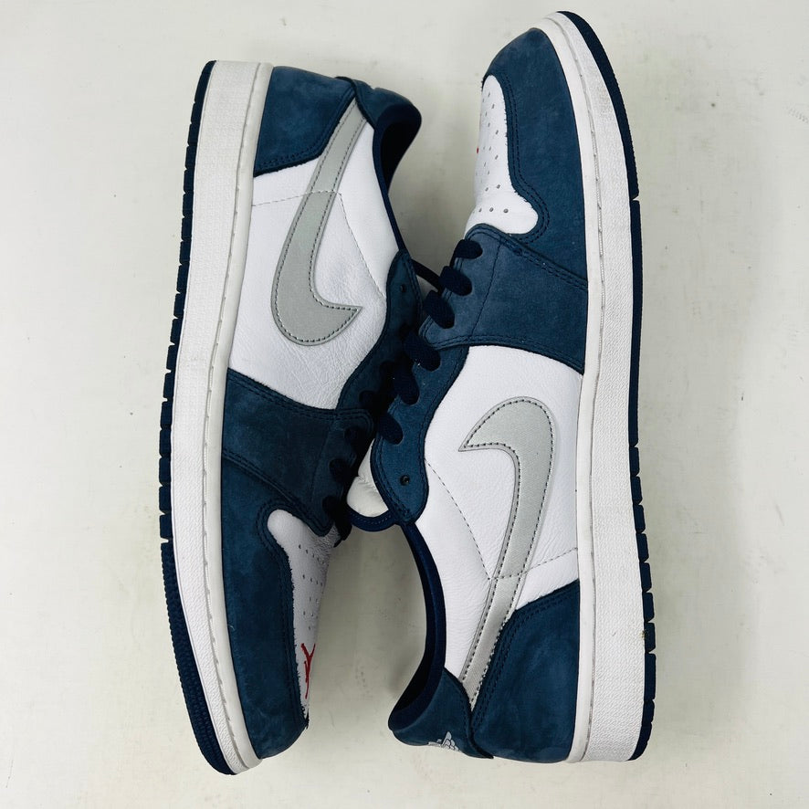 The Jordan 1 Low SB Midnight Navy sneakers, with white and navy panels and a side Nike swoosh, are displayed on a pristine shoebox. A spare set of white laces featuring the Nike SB logo in Metallic Silver is also included.
