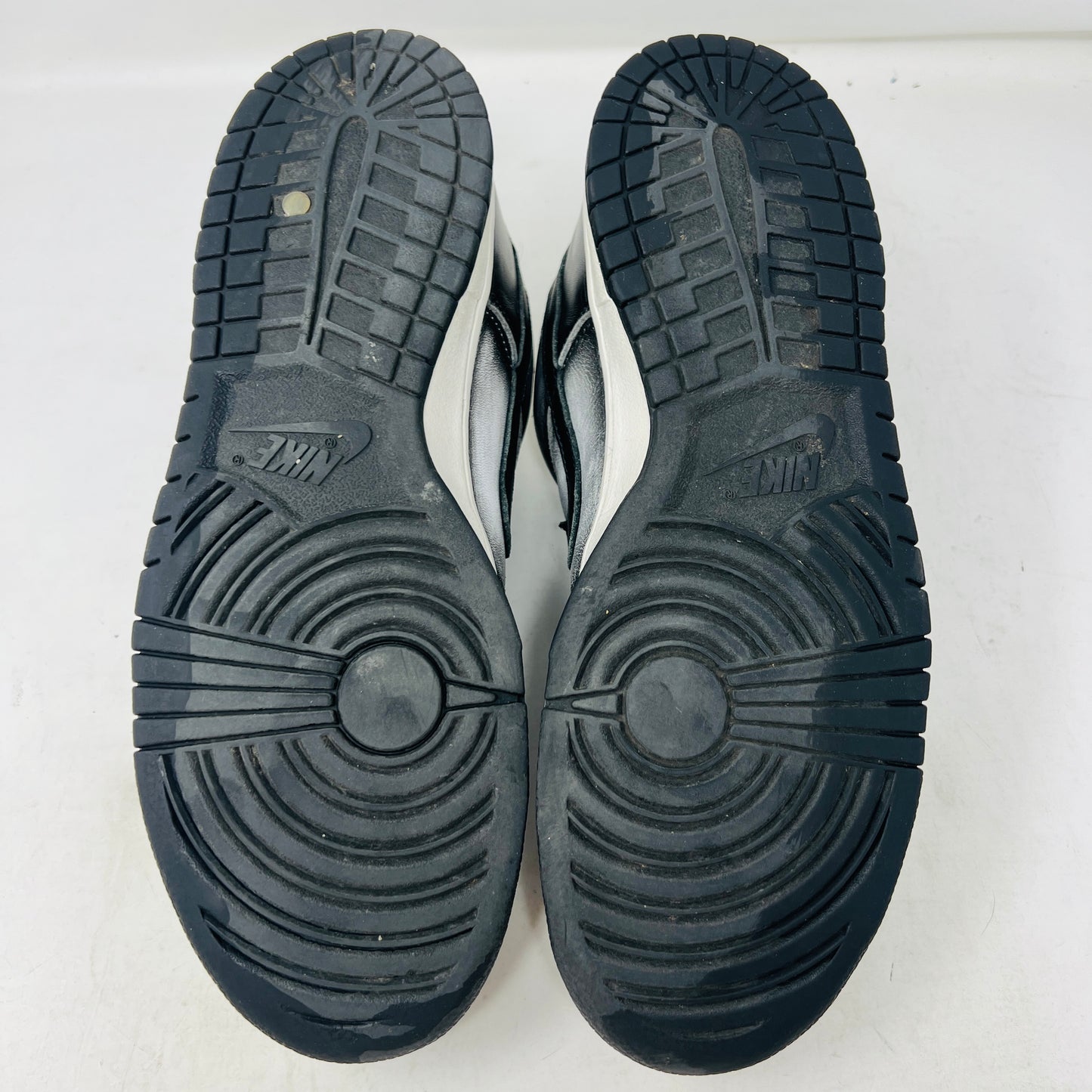 A pair of worn black and white Nike Dunk Low Haze sneakers with visible scuff marks rest on an orange Nike shoebox labeled size 10.5, featuring product details.