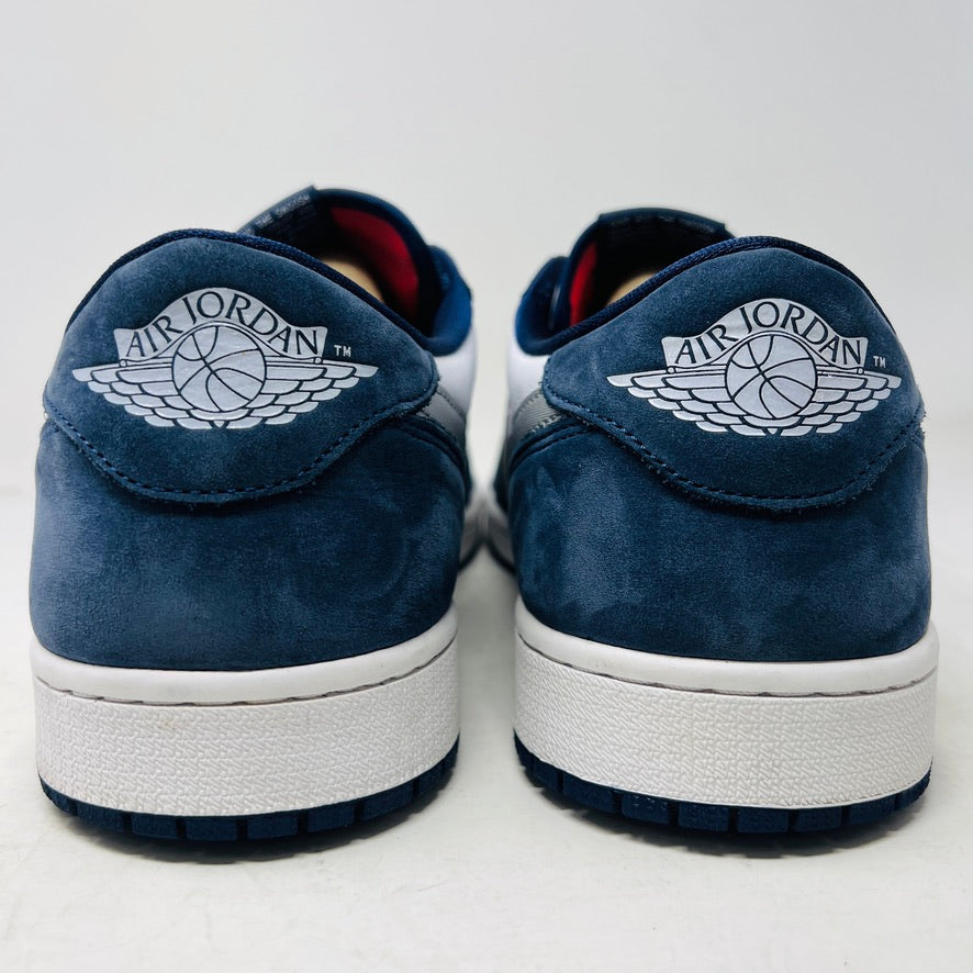 The Jordan 1 Low SB Midnight Navy sneakers, with white and navy panels and a side Nike swoosh, are displayed on a pristine shoebox. A spare set of white laces featuring the Nike SB logo in Metallic Silver is also included.