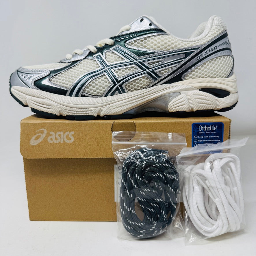 The ASICS GT-2160 Kith Cream Scarab is displayed on a brown box with two spare lace sets, striped and white, offering versatility. An Ortholite tag emphasizes comfort while its clean white and black uppers ensure it complements any outfit effortlessly.