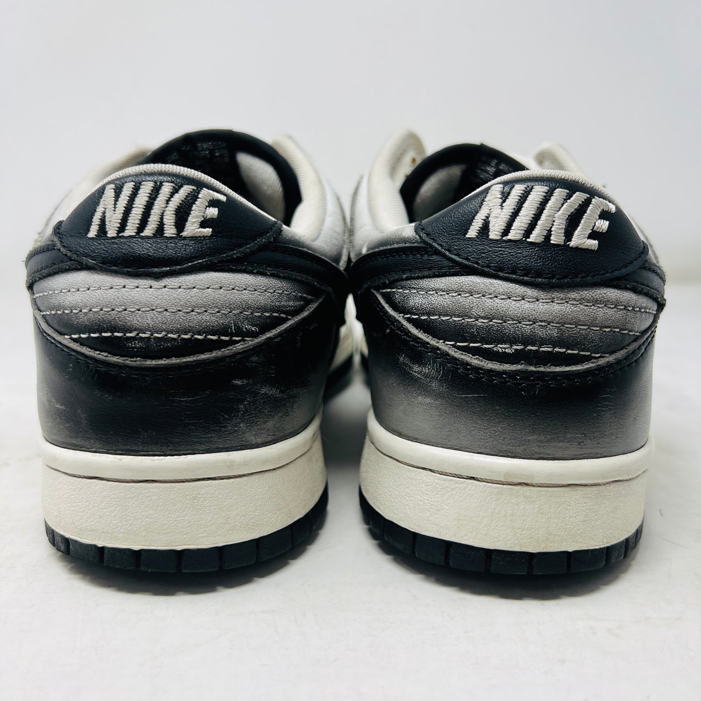 A pair of worn black and white Nike Dunk Low Haze sneakers with visible scuff marks rest on an orange Nike shoebox labeled size 10.5, featuring product details.