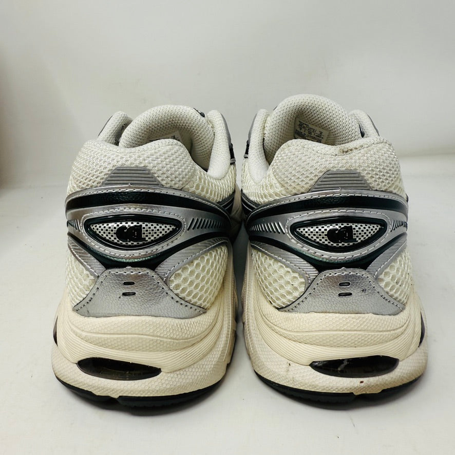 The ASICS GT-2160 Kith Cream Scarab is displayed on a brown box with two spare lace sets, striped and white, offering versatility. An Ortholite tag emphasizes comfort while its clean white and black uppers ensure it complements any outfit effortlessly.