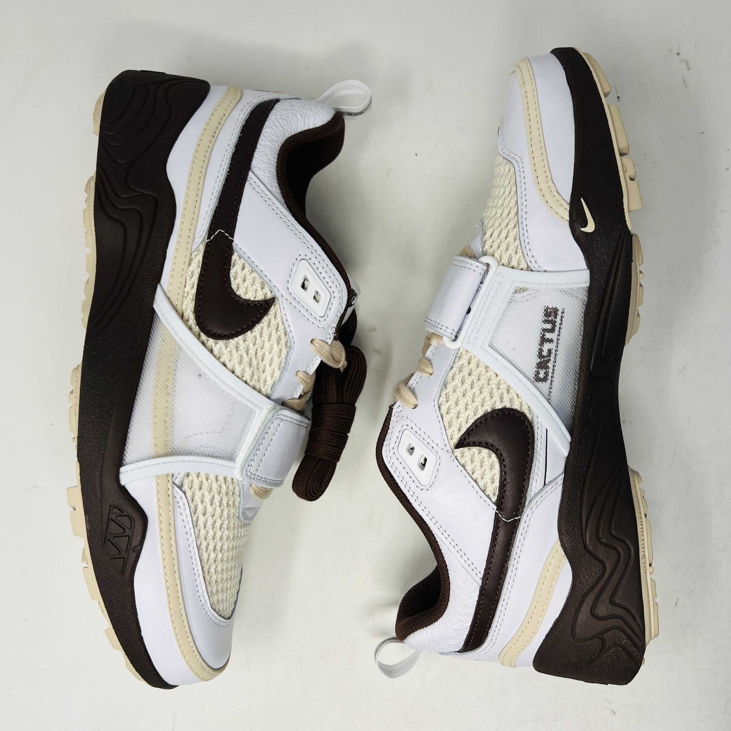 The Nike Zoom Field Jaxx Travis Scott Light Chocolate sneaker showcases a white and brown design with mesh and leather textures, Velcro strap, brown laces, and a prominent brown swoosh. It sits on a blue Nike shoebox.