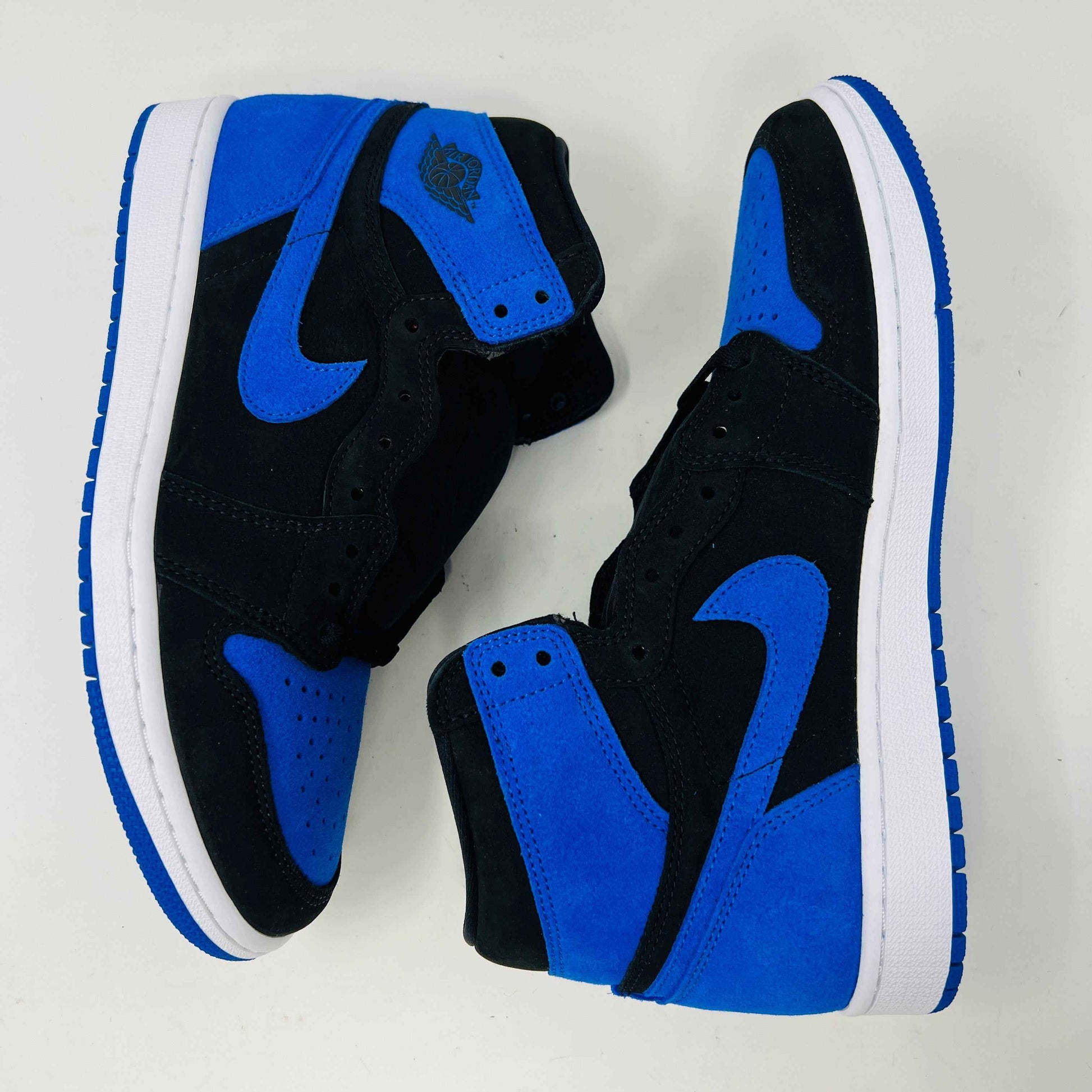 A pair of new Jordan 1 Retro High OG Royal Reimagined sneakers by Jordan rests on a matching box. These genuine shoes have blue accents on the swoosh, heel, and toe cap with a white midsole. The box also features a blue Nike logo.