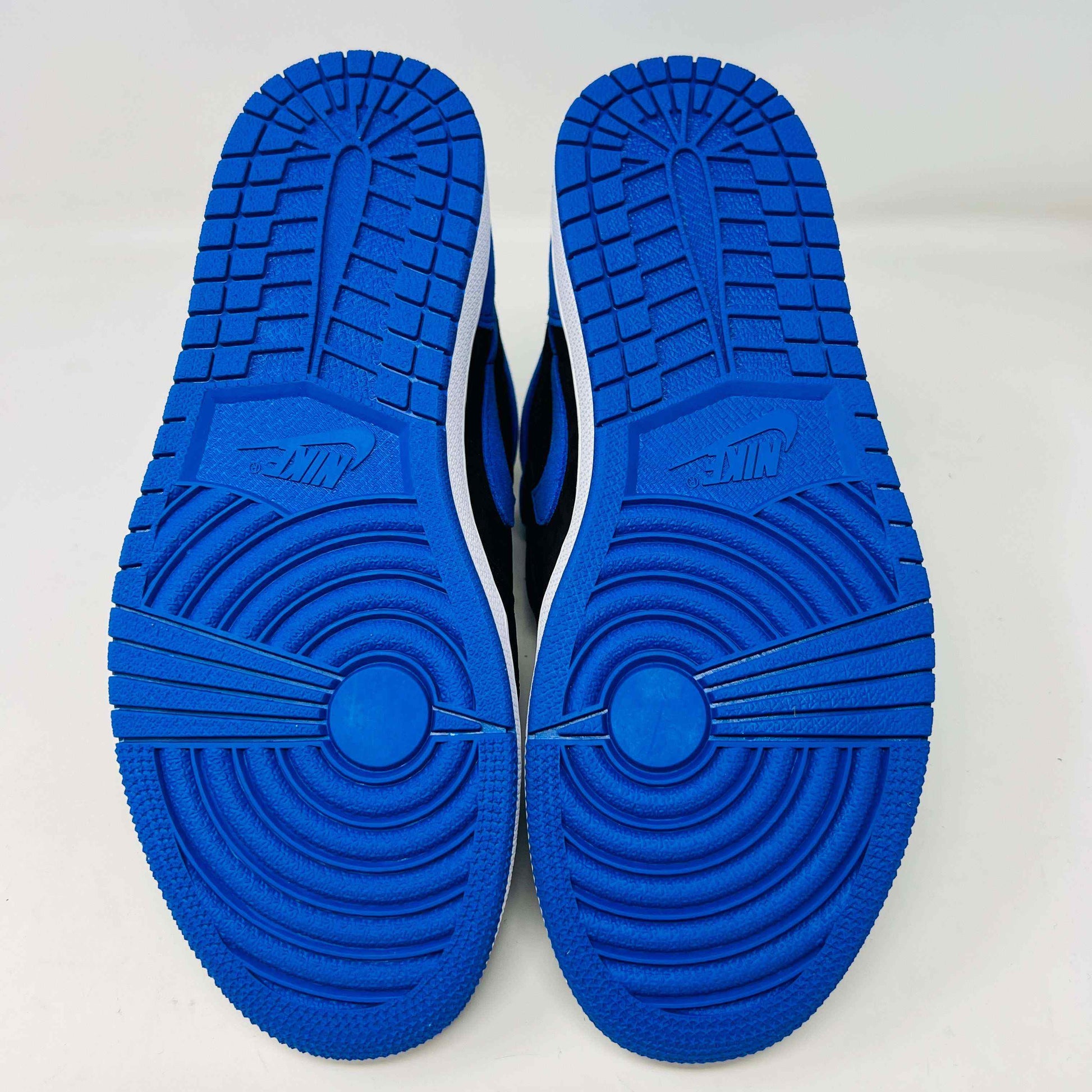 A pair of new Jordan 1 Retro High OG Royal Reimagined sneakers by Jordan rests on a matching box. These genuine shoes have blue accents on the swoosh, heel, and toe cap with a white midsole. The box also features a blue Nike logo.