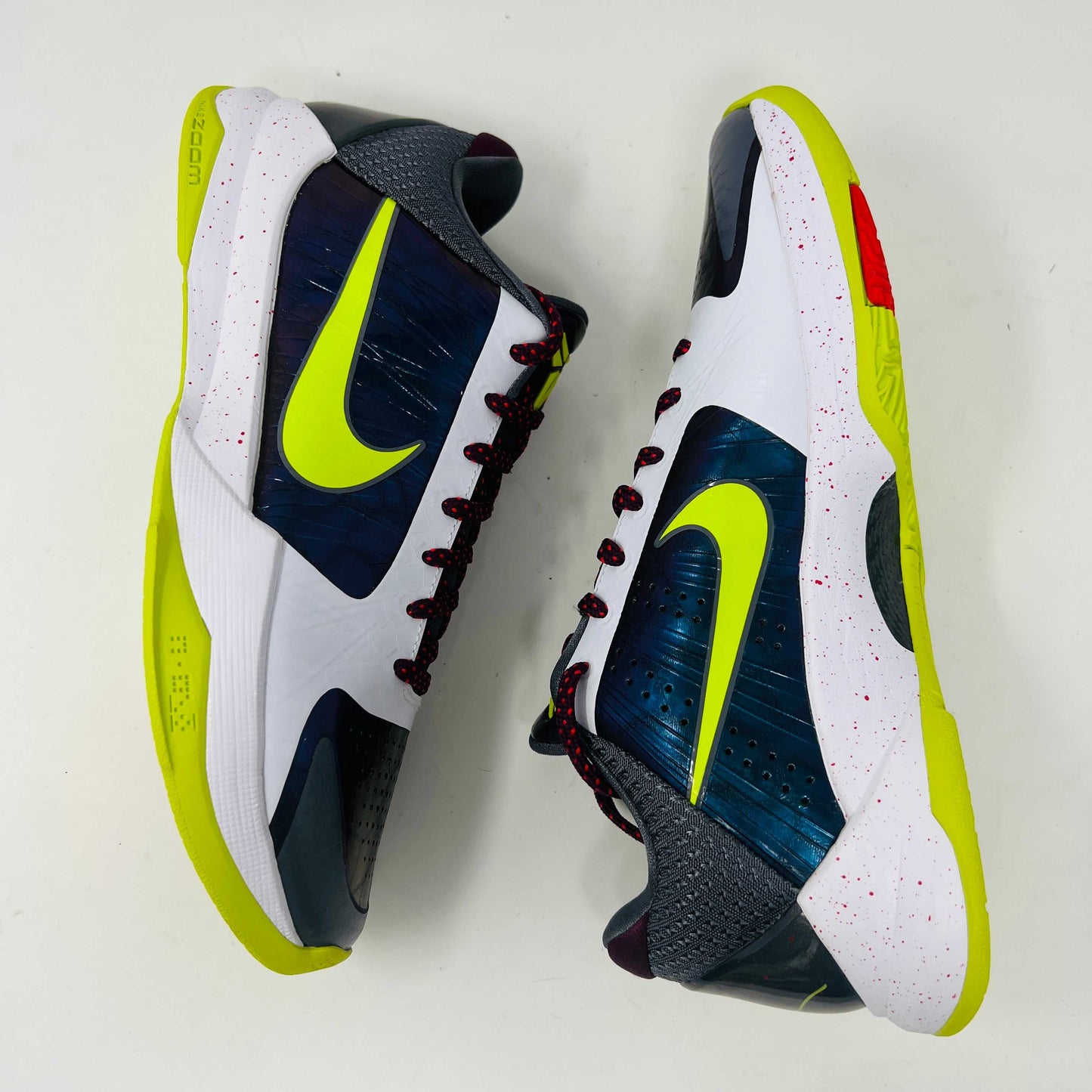 The Nike Kobe 5 Protro Chaos sneaker features a white and purple upper, neon yellow swoosh, maroon laces, and a neon yellow sole with red speckles. It is brand new in its sleek black box.