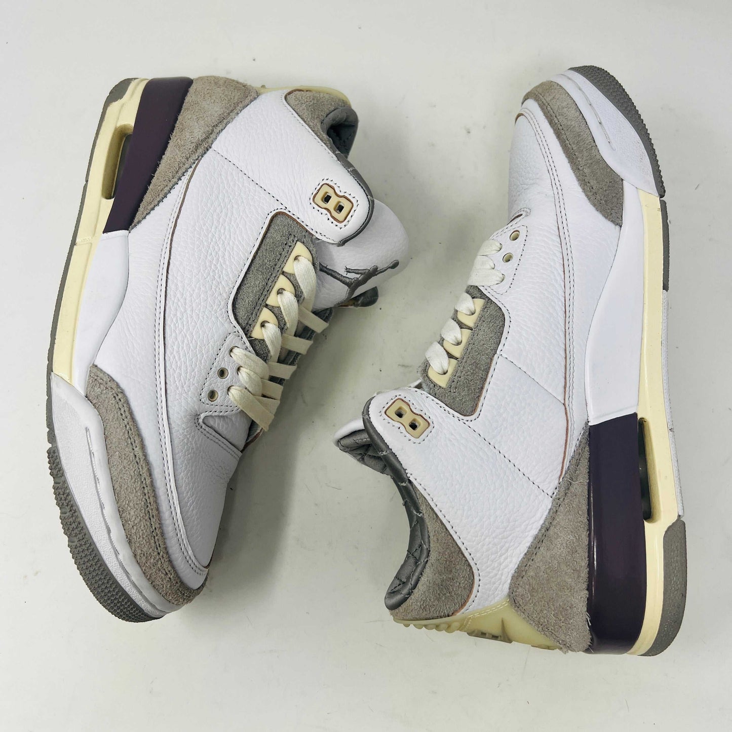 The Holy Ground Jordan 3 Retro SP A Ma Maniére (Womens) sneakers in white and gray, priced at $450, are displayed atop their box. They feature textured leather, suede accents, and include a pack of cream-colored extra laces for customization.