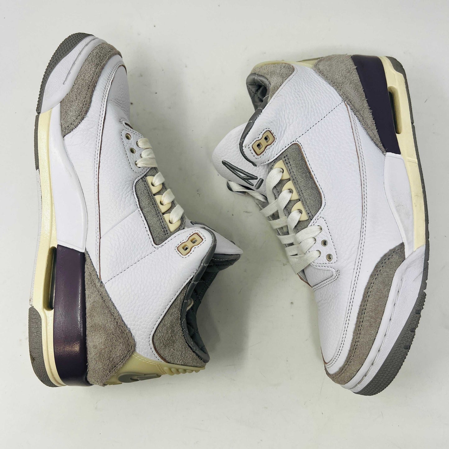 The Holy Ground Jordan 3 Retro SP A Ma Maniére (Womens) sneakers in white and gray, priced at $450, are displayed atop their box. They feature textured leather, suede accents, and include a pack of cream-colored extra laces for customization.