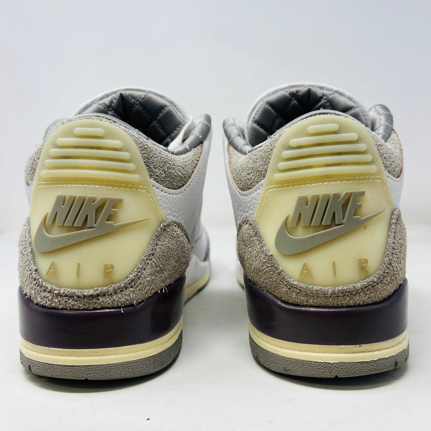 The Holy Ground Jordan 3 Retro SP A Ma Maniére (Womens) sneakers in white and gray, priced at $450, are displayed atop their box. They feature textured leather, suede accents, and include a pack of cream-colored extra laces for customization.