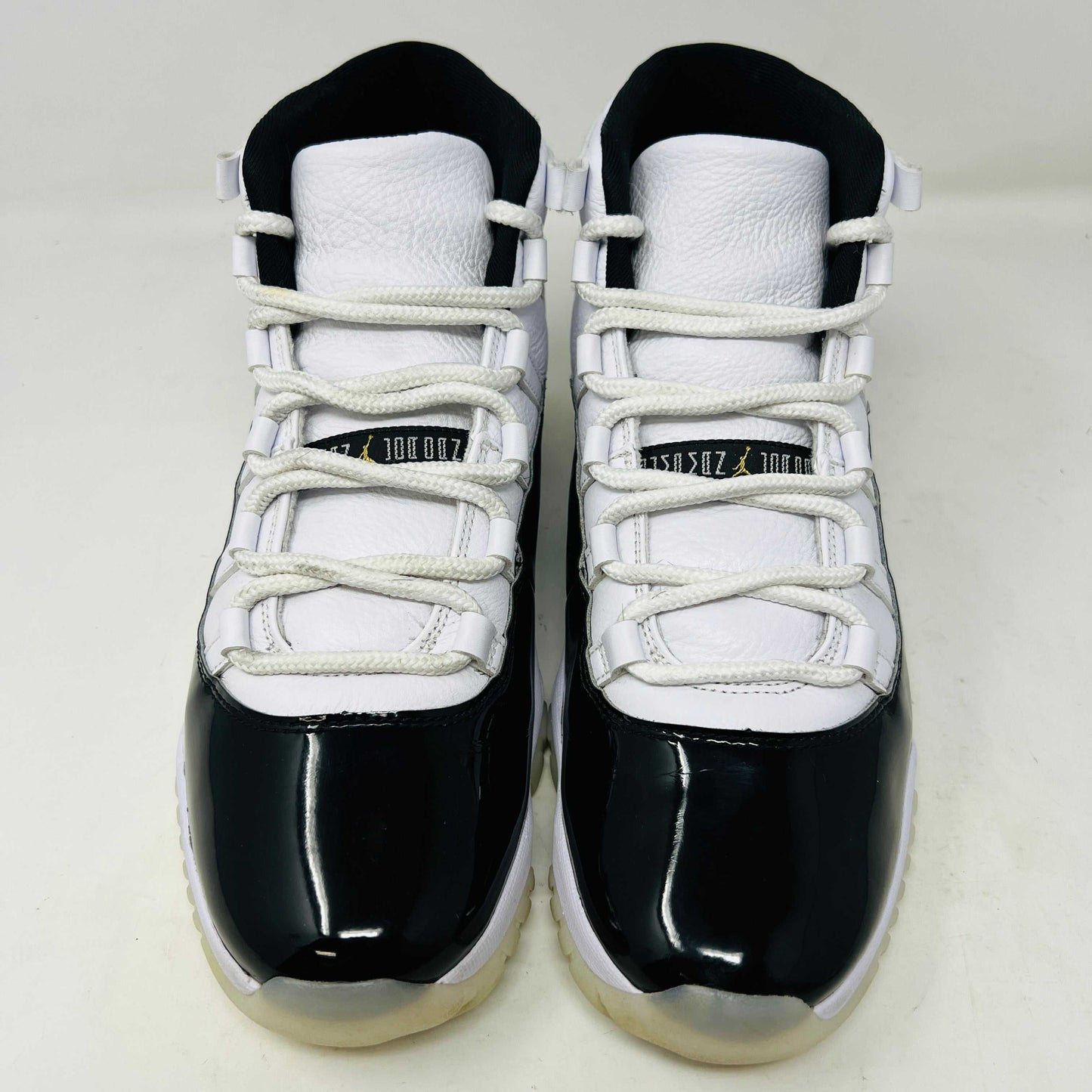 The Jordan 11 Retro DMP Gratitude (2023) sneaker, featuring white mesh, black patent leather, a translucent sole, and a gold Jumpman logo on the heel, rests elegantly on its box labeled with size and model details.