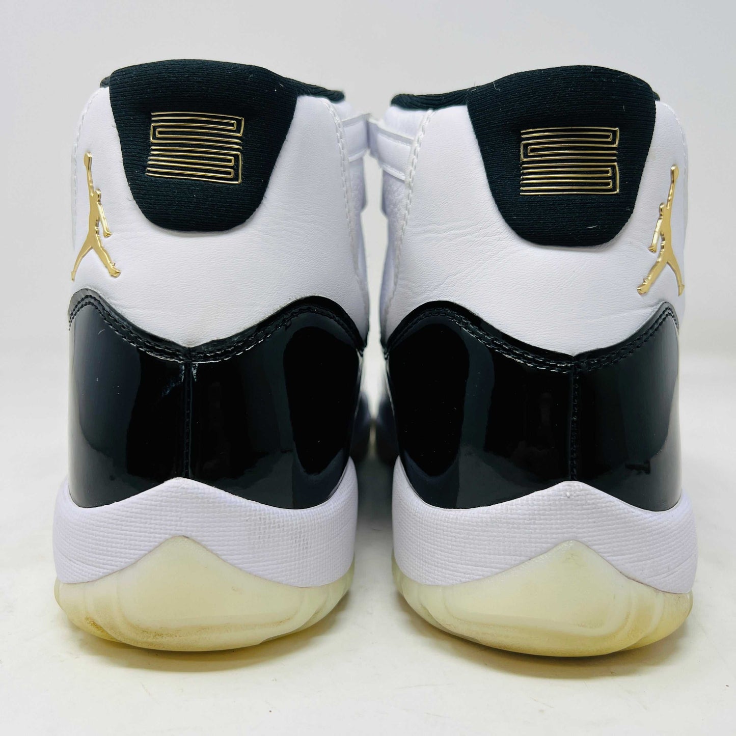 The Jordan 11 Retro DMP Gratitude (2023) sneaker, featuring white mesh, black patent leather, a translucent sole, and a gold Jumpman logo on the heel, rests elegantly on its box labeled with size and model details.