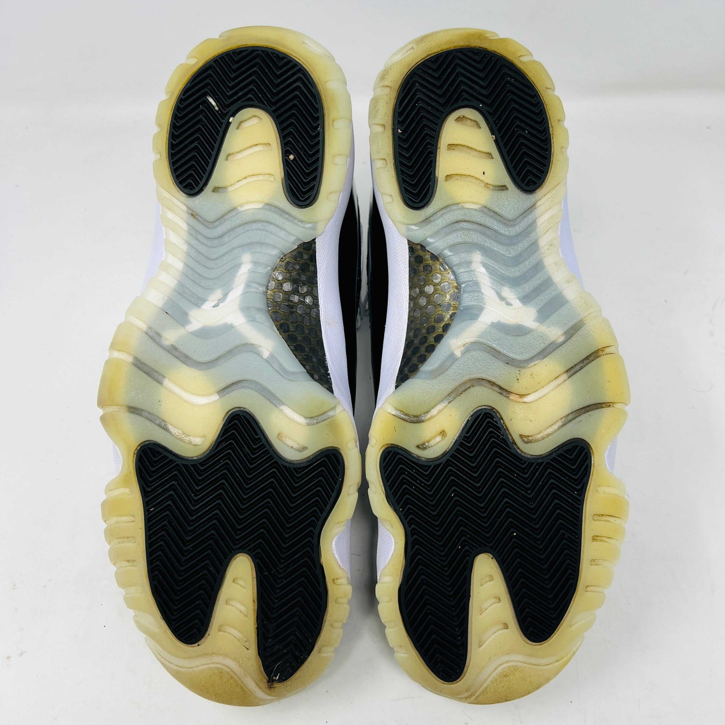 The Jordan 11 Retro DMP Gratitude (2023) sneaker, featuring white mesh, black patent leather, a translucent sole, and a gold Jumpman logo on the heel, rests elegantly on its box labeled with size and model details.