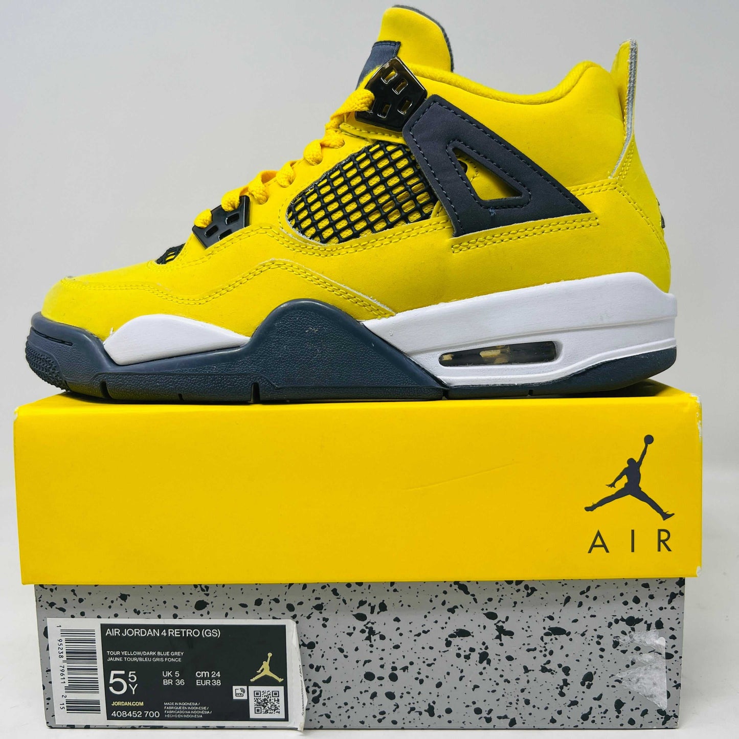 Jordan 4 Retro Lightning 2021 GS sneaker on yellow box with visible scuffs and slight heel drag.