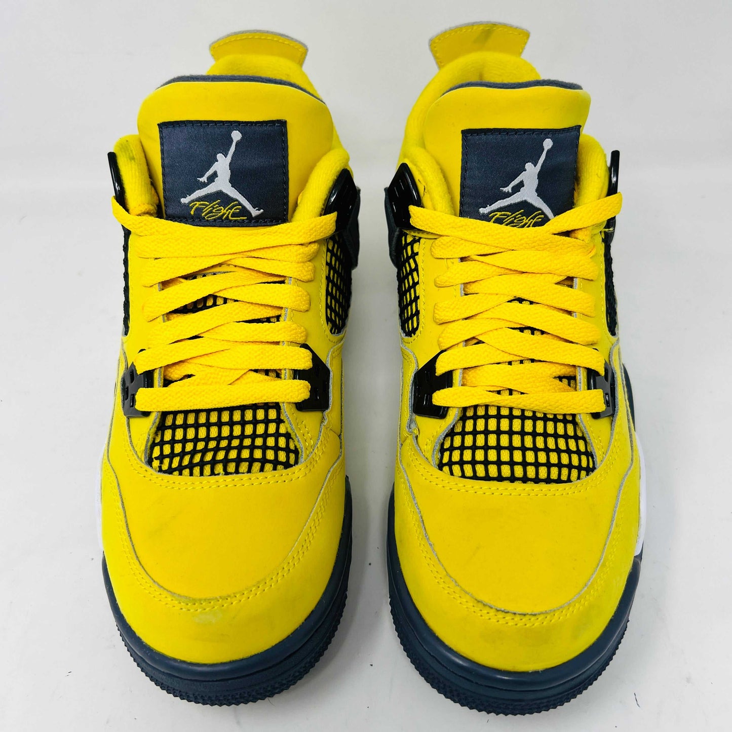 A genuine pair of Jordan 4 Retro Lightning (2021) (GS) in yellow and navy sits on a matching box with a speckled gray base, featuring mesh details, white accents, and the iconic Jumpman logo alongside product info.