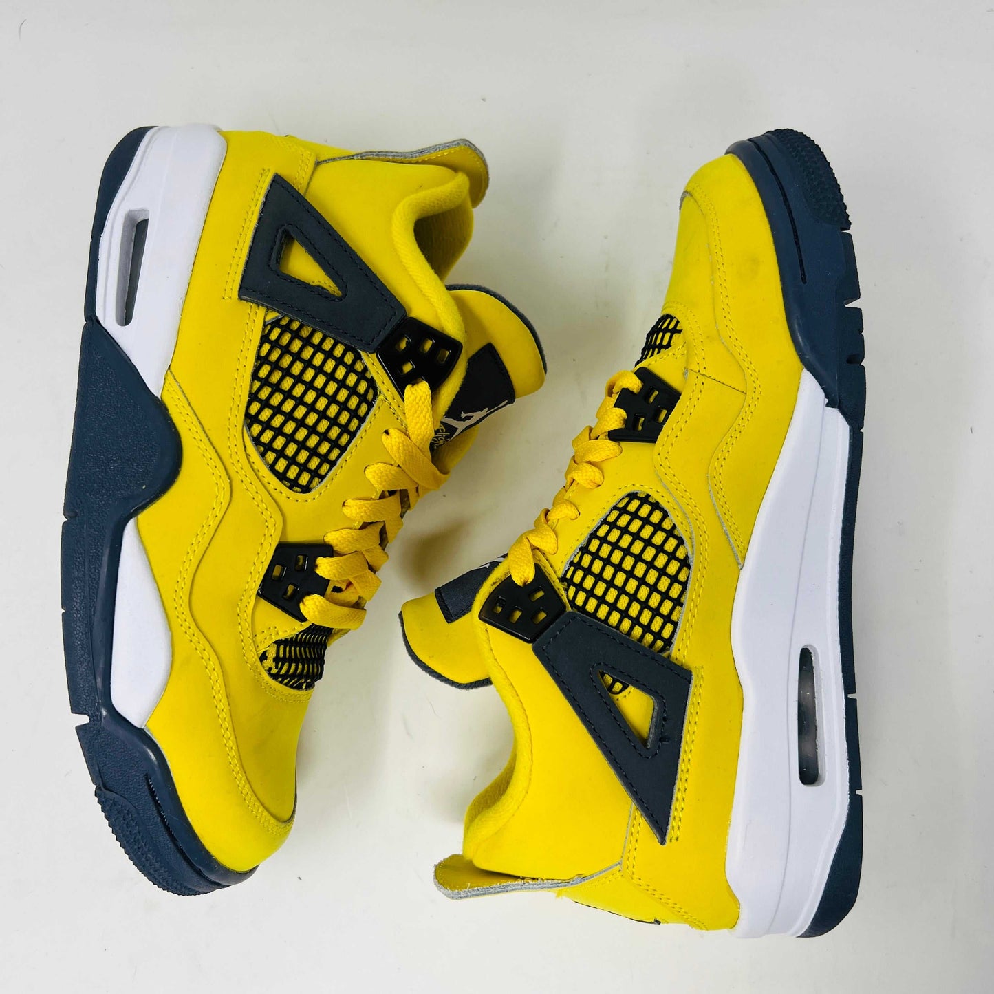 A genuine pair of Jordan 4 Retro Lightning (2021) (GS) in yellow and navy sits on a matching box with a speckled gray base, featuring mesh details, white accents, and the iconic Jumpman logo alongside product info.
