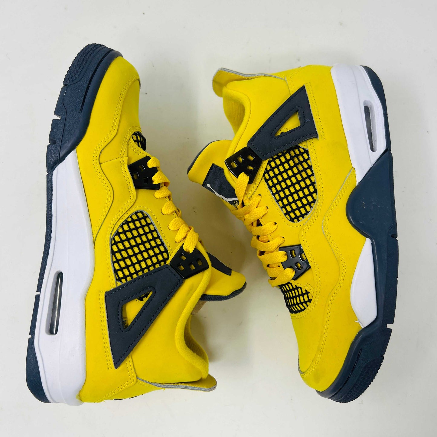 A genuine pair of Jordan 4 Retro Lightning (2021) (GS) in yellow and navy sits on a matching box with a speckled gray base, featuring mesh details, white accents, and the iconic Jumpman logo alongside product info.