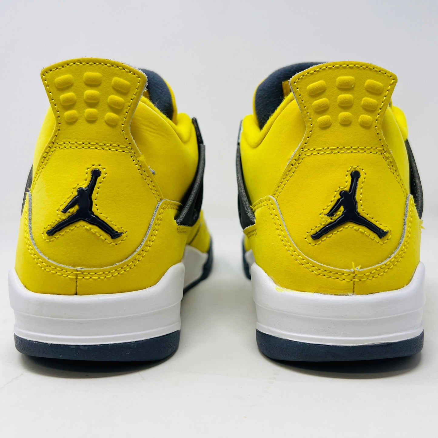 A genuine pair of Jordan 4 Retro Lightning (2021) (GS) in yellow and navy sits on a matching box with a speckled gray base, featuring mesh details, white accents, and the iconic Jumpman logo alongside product info.