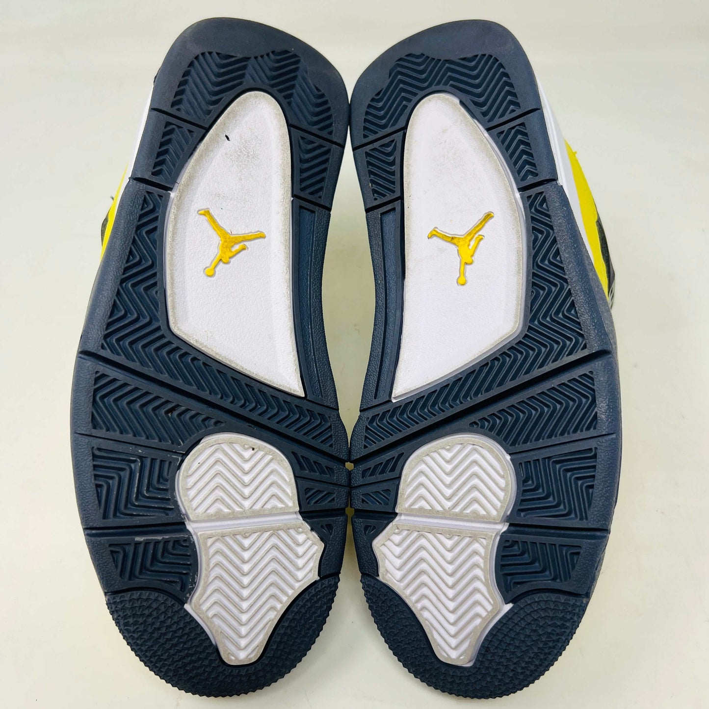 A genuine pair of Jordan 4 Retro Lightning (2021) (GS) in yellow and navy sits on a matching box with a speckled gray base, featuring mesh details, white accents, and the iconic Jumpman logo alongside product info.