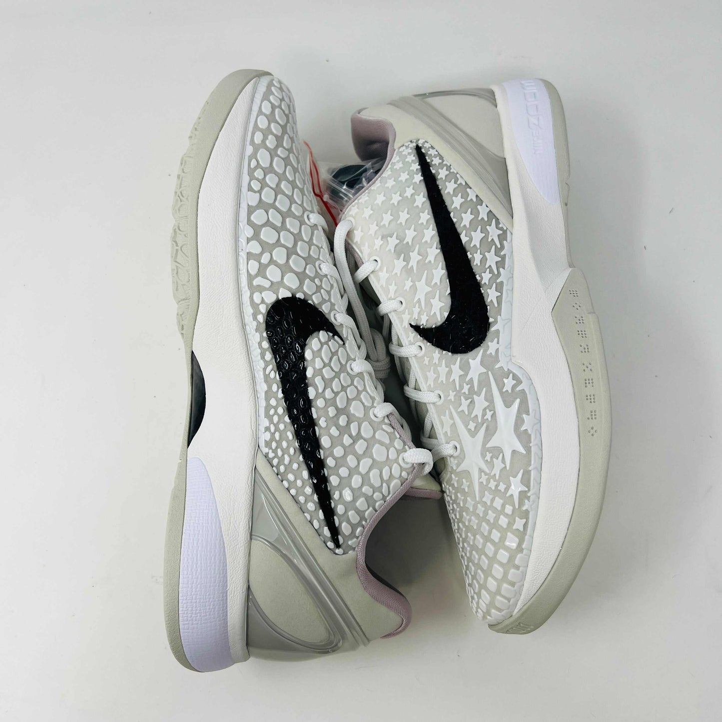 The Nike Kobe 6 Protro Sail All-Star shoes, featuring white textured patterns and black swoosh details with star designs, are elegantly displayed on a sleek black shoebox.