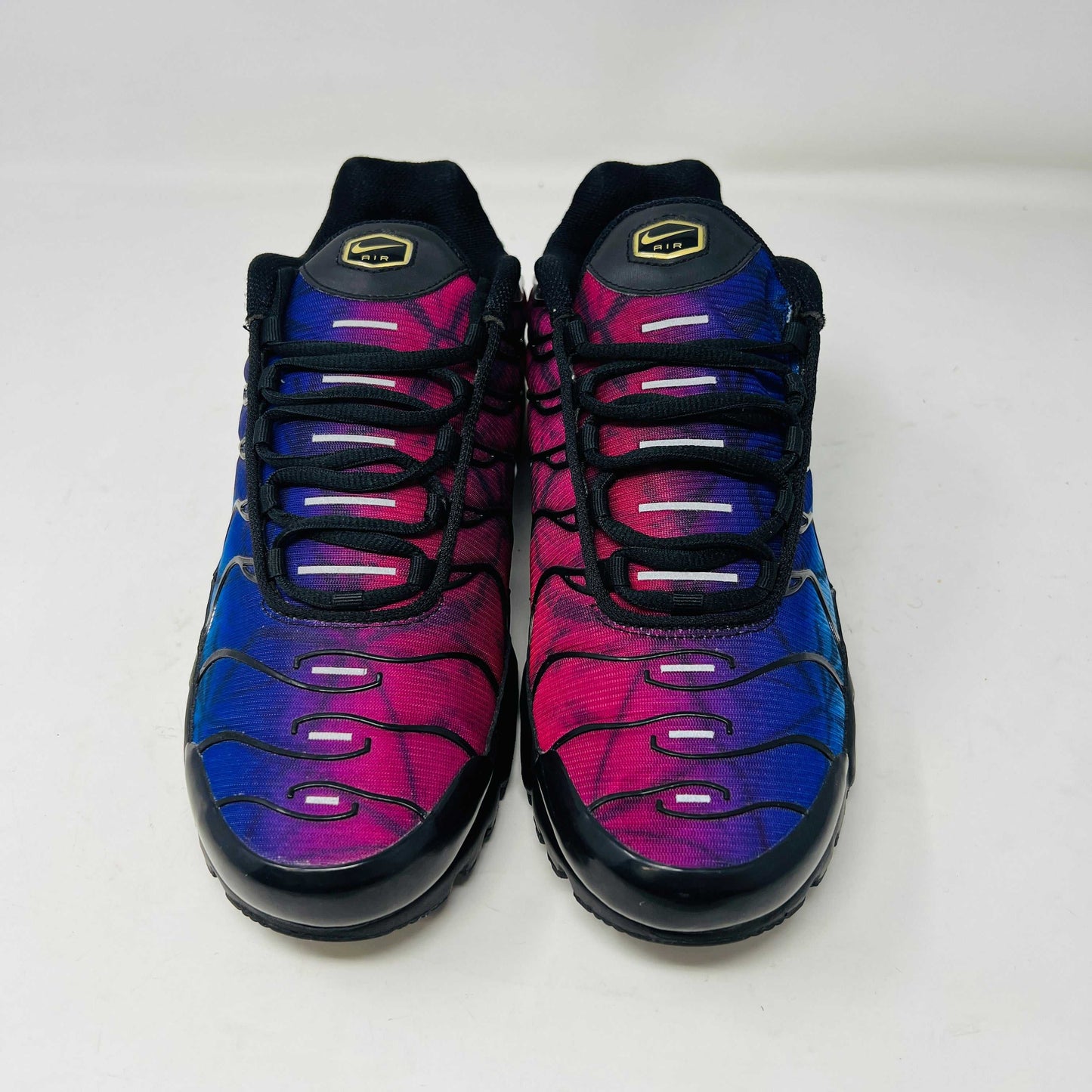 A pair of Nike Air Max Plus 25th Anniversary sneakers, featuring a blue and black wavy color pattern, sits atop a black shoebox. These authentic shoes boast the iconic Nike swoosh and visible air cushioning in the sole.
