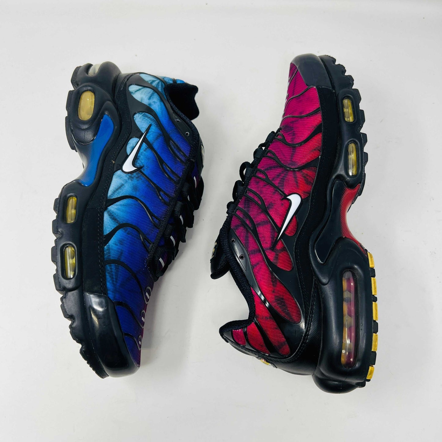 A pair of Nike Air Max Plus 25th Anniversary sneakers, featuring a blue and black wavy color pattern, sits atop a black shoebox. These authentic shoes boast the iconic Nike swoosh and visible air cushioning in the sole.