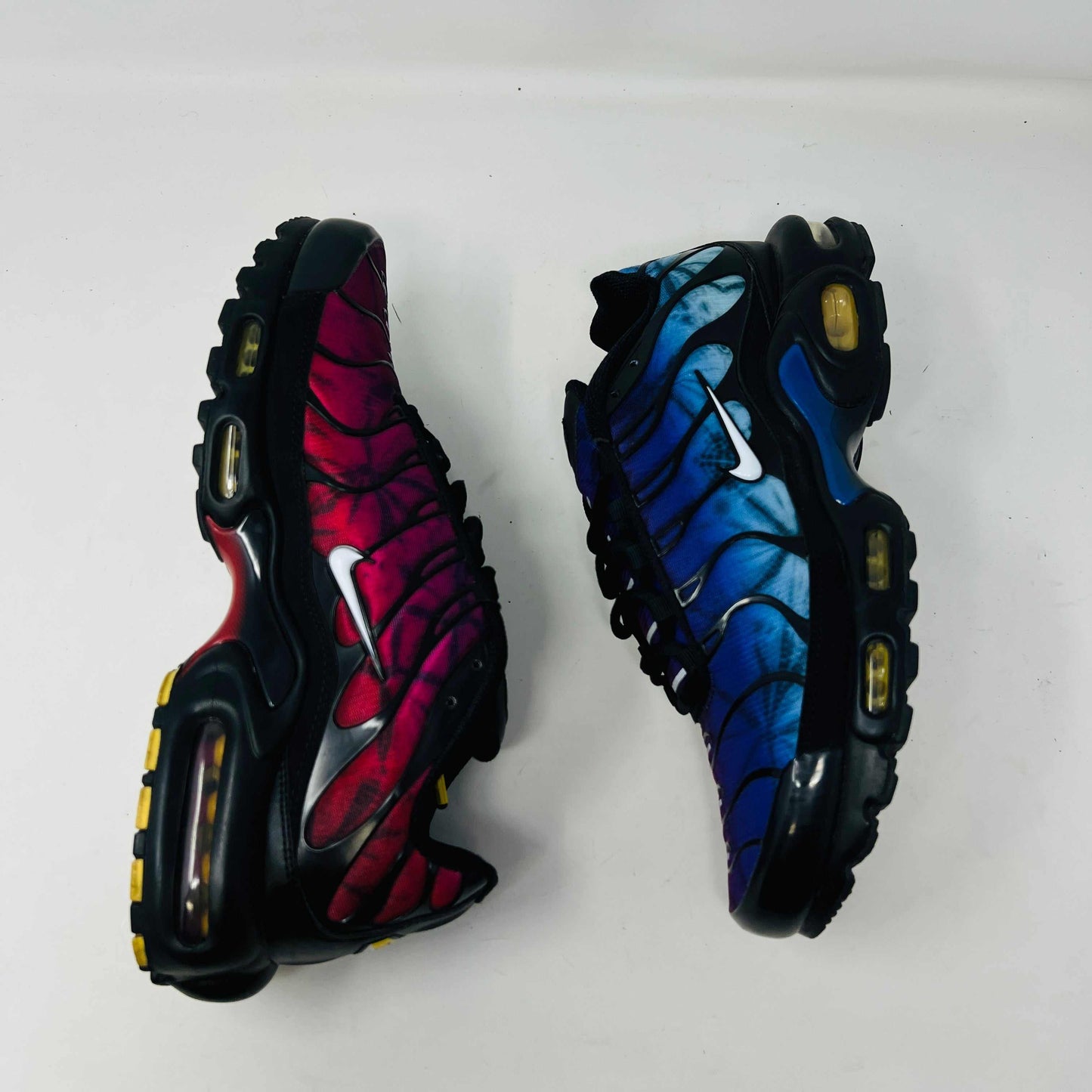 A pair of Nike Air Max Plus 25th Anniversary sneakers, featuring a blue and black wavy color pattern, sits atop a black shoebox. These authentic shoes boast the iconic Nike swoosh and visible air cushioning in the sole.