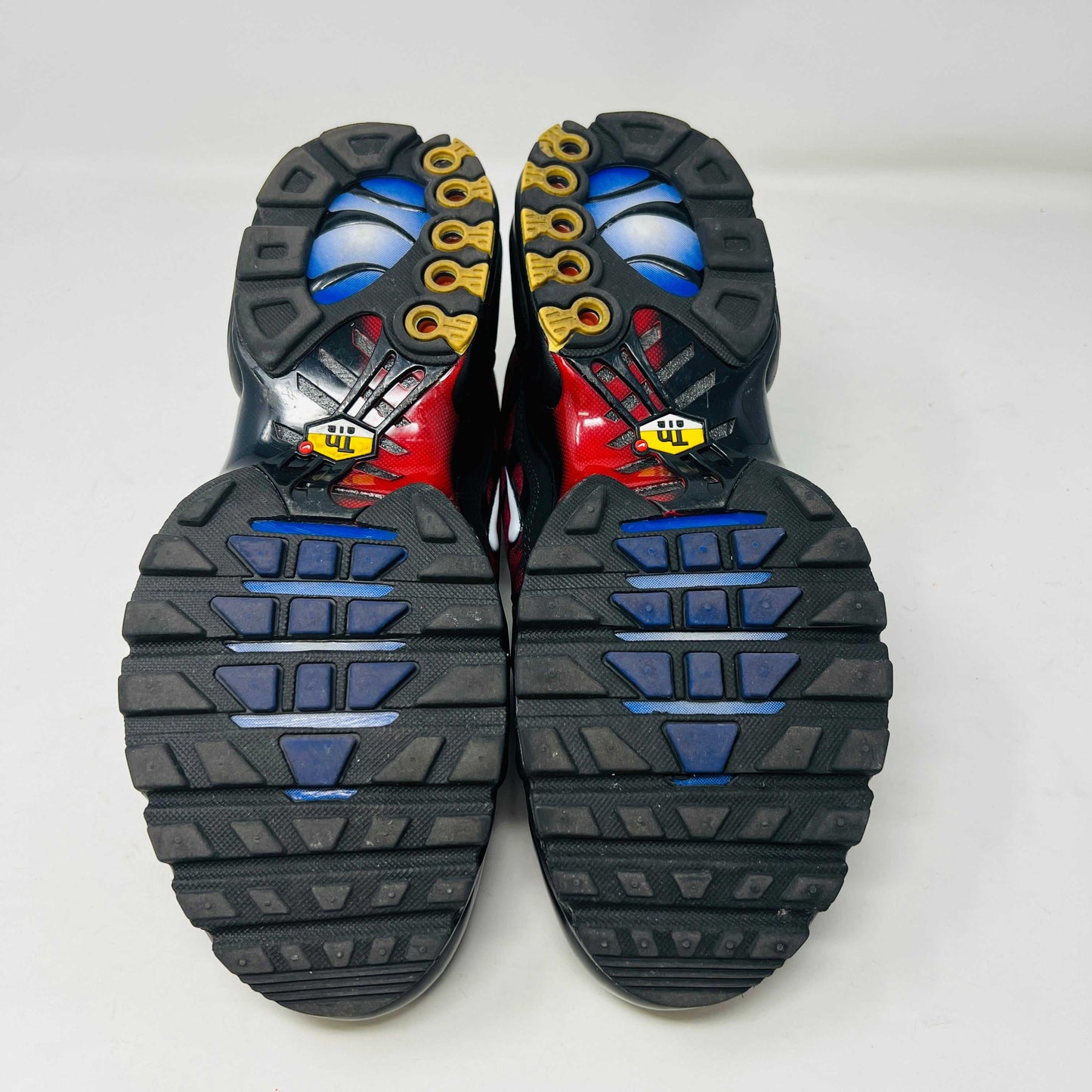 A pair of Nike Air Max Plus 25th Anniversary sneakers, featuring a blue and black wavy color pattern, sits atop a black shoebox. These authentic shoes boast the iconic Nike swoosh and visible air cushioning in the sole.