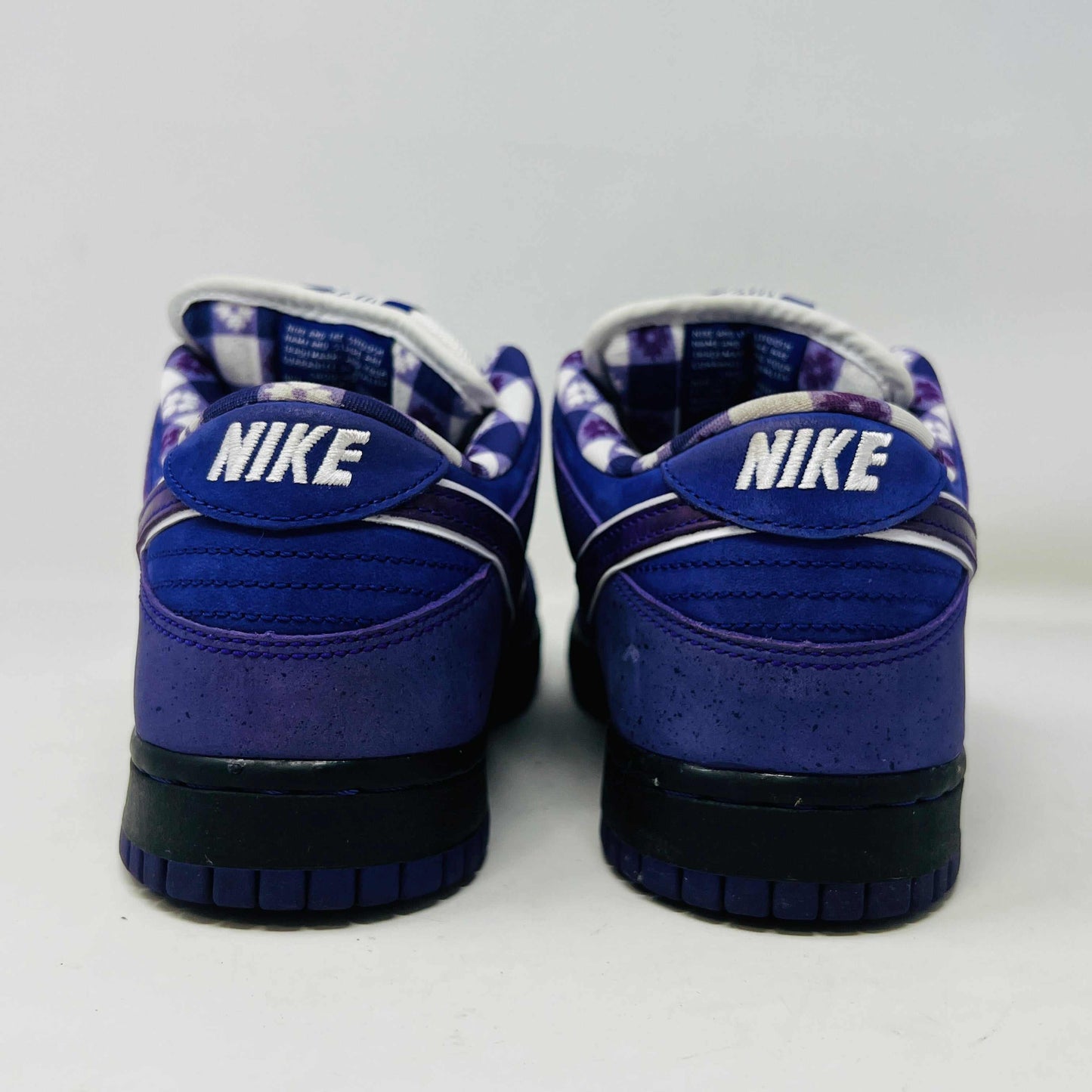 The Nike SB Dunk Low Concepts Purple Lobster sneaker, featuring a clean upper with a white swoosh, rests on a blue and white Nike SB shoebox. An extra bag with pink laces adds a vibrant touch in front of the box.