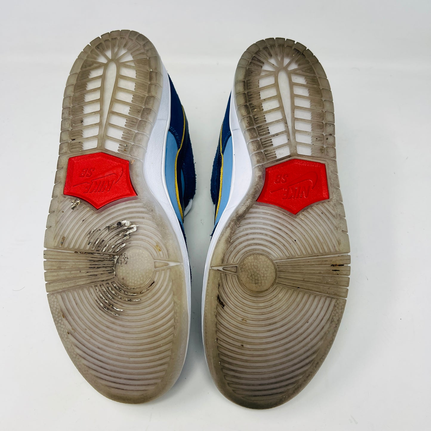 A Nike SB Dunk Low Pro Why So Sad? shoe, with blue uppers and white sole, rests on a purple box. It features an embroidered graphic on the heel, a dark blue swoosh, and extra laces in front. Price tags from 2022 are visible beside it.